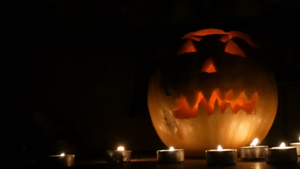 暗闇の中で多くのキャンドルに囲まれた恐ろしいハロウィンかぼちゃ - 映像、動画