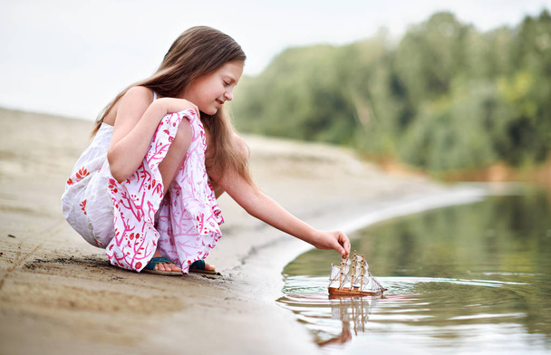 meisje speelt met een toy zeilschip door de rivier - Foto, afbeelding