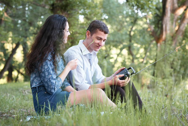 young couple sitting on the grass in the forest and looking on sunset, listen to radio, summer nature, bright sunlight, shadows and green leaves, romantic feelings - Photo, image
