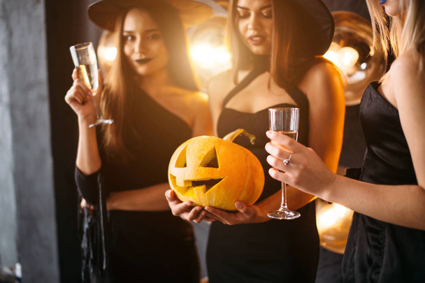 three cheerful young women in witch halloween costumes with pumpkin - Valokuva, kuva