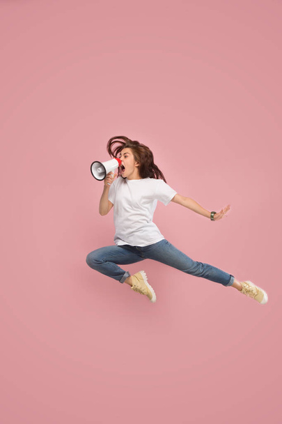 Beautiful young woman jumping with megaphone isolated over pink background - Φωτογραφία, εικόνα