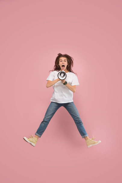 Beautiful young woman jumping with megaphone isolated over pink background - Photo, image