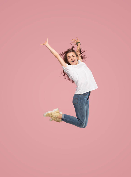 Freedom in moving. Pretty young woman jumping against pink background - Fotó, kép
