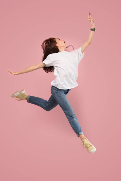 Full length of pretty young woman with mobile phone while jumping - Foto, imagen