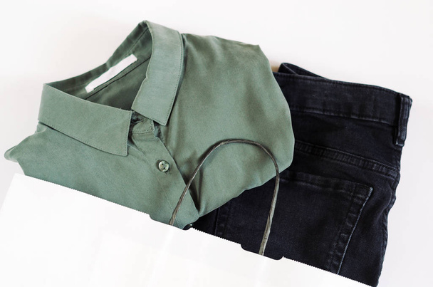 白タグと白い背景の紙の袋に黒いジーンズと緑のシャツ。ショッピング、購入服、ファッションのコンセプト. - 写真・画像