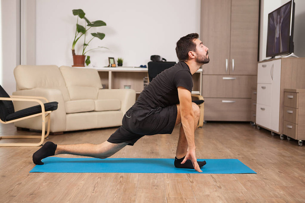 Fit man in his 30s doing yoga on a mattress in his house - Photo, Image