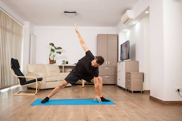 Привлекательный человек пытается расширить сторону йоги позы на полу его дома
 - Фото, изображение