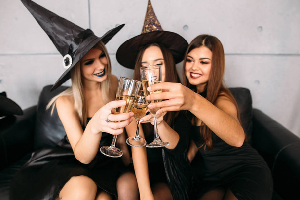 In good moods at halloween party. womans sitting on sofa and drink champagne - 写真・画像