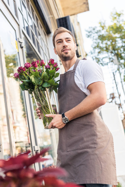low angle view of florist holding glass jar with burgundy roses near flower shop - Photo, Image