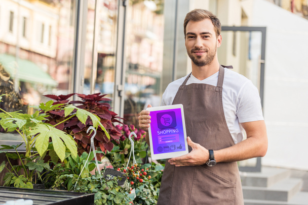 handsome florist holding tablet with shopping appliance near flower shop - Photo, Image