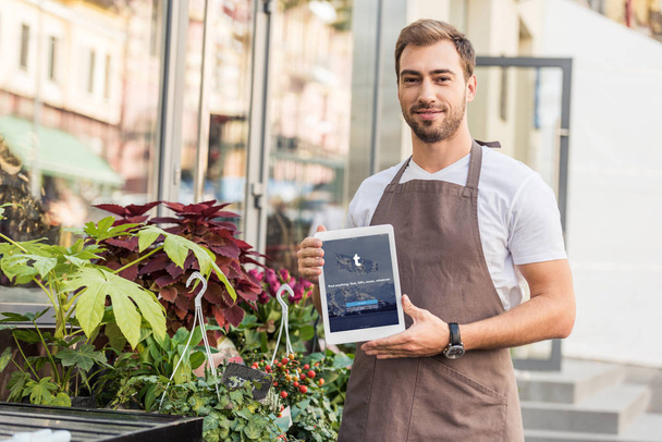 handsome florist holding tablet with loaded tumblr page near flower shop - Photo, Image