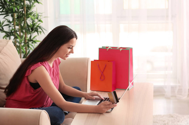jonge vrouw online winkelen met creditcard en laptop thuis - Foto, afbeelding