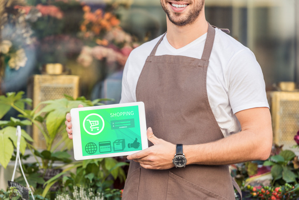 cropped image of smiling florist holding tablet with shopping appliance near flower shop - Photo, Image