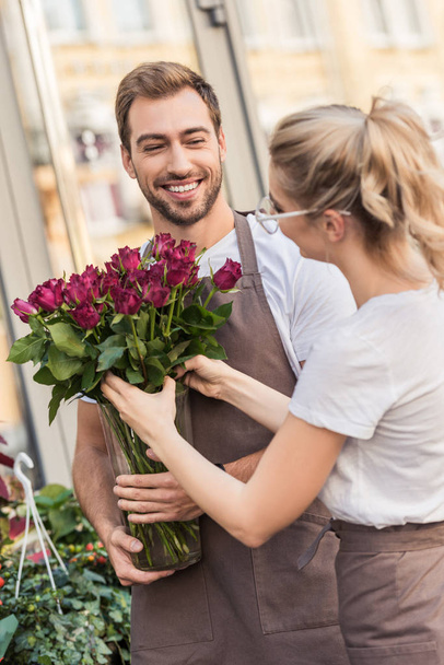 happy young florists holding burgundy roses near flower shop - Photo, Image