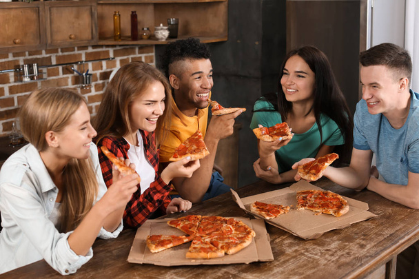 Νέοι διασκεδάζουν στο κόμμα με νόστιμη πίτσα σε εσωτερικούς χώρους - Φωτογραφία, εικόνα