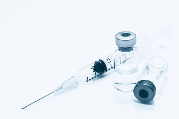 Injektiopullo lääke- tai rokotetta ja 3 ml muovinen ruisku, jossa neula valkoisella pohjalla, sininen sävy
 - Valokuva, kuva