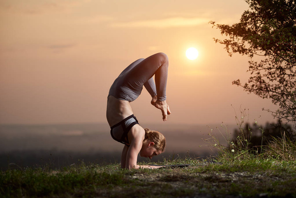 Güçlü kas esnek yalınayak kadın eğitim kıyafeti zor işi karmaşık yoga egzersizleri hafif pembe yaz sabah gökyüzü kopya alan arka plan açık havada üzerinde. Fitness ve güzellik kavramı. - Fotoğraf, Görsel