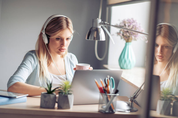 Jonge vrouw die werkt met koptelefoon vanuit kantoor aan huis - Foto, afbeelding