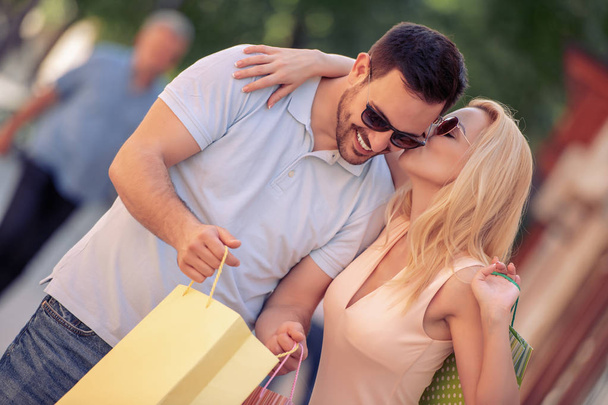 hermosa pareja feliz con bolsas de compras después de ir de compras en la ciudad sonriendo y besándose a la luz del día
 - Foto, Imagen