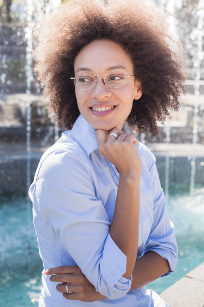 Leuke mooie jonge zwarte vrouw, gezicht lachend, afro kapsel, draagt een bril en casual kleding, vrouwelijke met een donkere huid, kijkend naar kant - Foto, afbeelding
