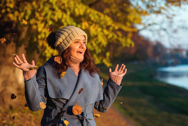 Ευτυχισμένη γυναίκα Έχοντας διασκέδαση με το φθινόπωρο φύλλα σε εξωτερικούς χώρους. Μόδα γυναίκα. Φθινόπωρο εποχή. Νεαρή γυναίκα ταξιδεύει το φθινόπωρο. Τρόπου ζωής, άνθρωποι, ταξίδι έννοια - Φωτογραφία, εικόνα