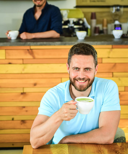 Man bearded guy drinks cappuccino wooden table cafe. Cafe visitor smiling face enjoy coffee drink. Many ways to enjoy coffee. Drink it black with milk or cream hot or cold. Add flavor or sweeteners - 写真・画像