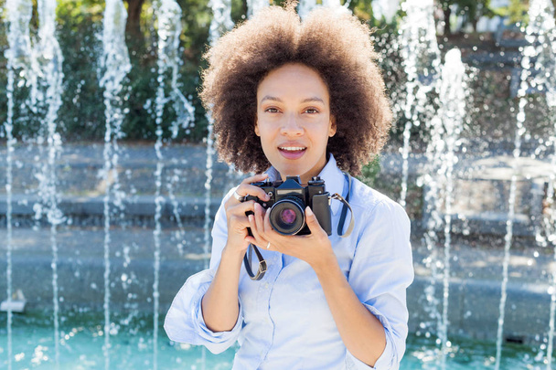 Porträt einer charmanten schwarzen Frau mit Retro-Kamera, Fotografin im Freien, Afro-Frisur, trägt lässige Kleidung, schaut in die Kamera - Foto, Bild