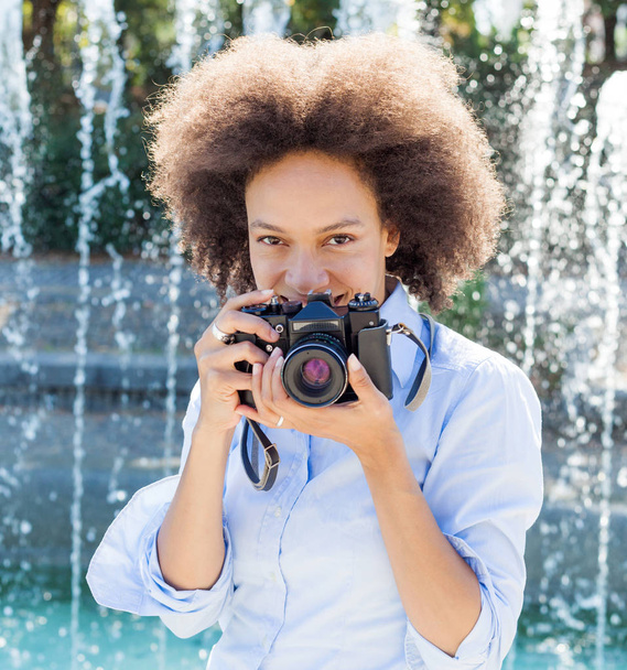 Portrait of charming black woman with retro camera, female photographer outdoor,afro hairstyle, wears casual clothes, looking at camera - Photo, Image