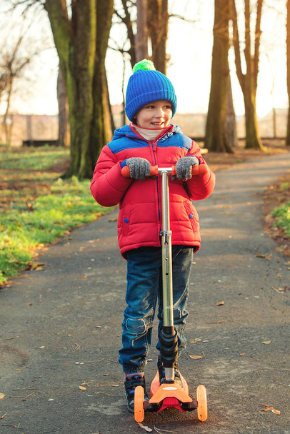 Šťastný chlapec se naučit jezdit na skútru v podzimním parku. Děti sport venku. Podzimní a zimní dětské módy. Šťastné a zdravé dětství. Legrační malý chlapec na koni scooter venku v chladném počasí - Fotografie, Obrázek