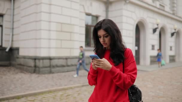 Woman using smartphone app walking in city, steadicam flying around her - Filmati, video