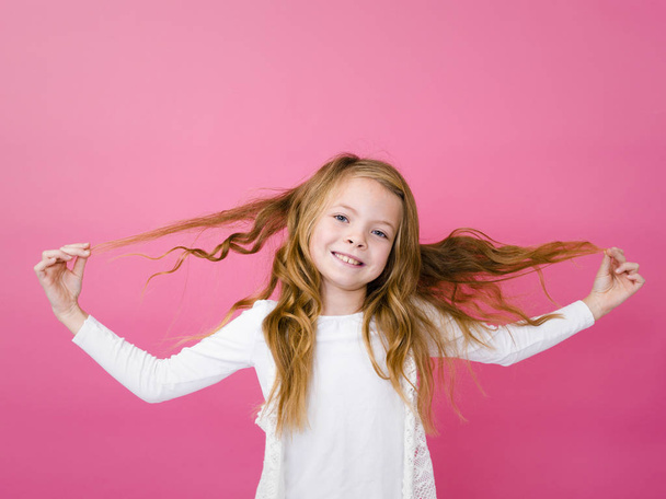 portrait of cheerful girl in white clothes jumping with raised hands over pink background  - Photo, Image