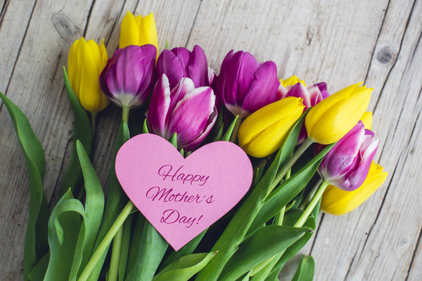 Pink and yellow tulips with text Happy mothers day on paper heart, close-up  - Photo, image