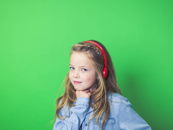 portrait of happy girl in red headphones listening music and smiling while looking at camera on green background    - Foto, Imagem