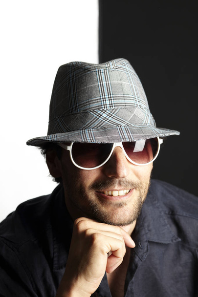 portrait of handsome man in hat and sunglasses toothy smiling and looking at camera on white and black background, close-up  - Fotó, kép