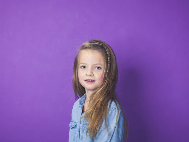 portrait of cute little girl wearing blue denim shirt in front of violet background in studio - Fotó, kép