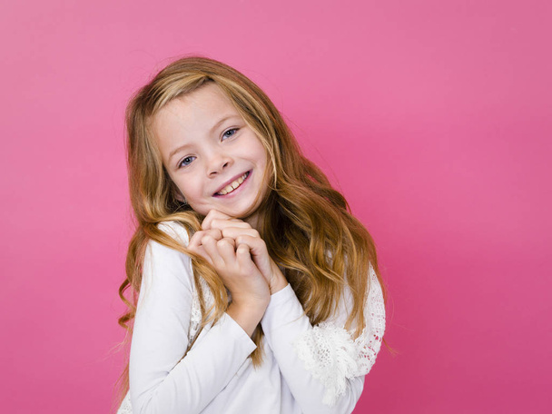 retrato de menina bonita em roupas brancas sorrindo e olhando para a câmera no fundo rosa
  - Foto, Imagem