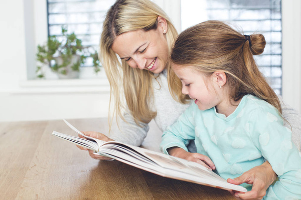 Mother with book teaching daughter to read at home  - Foto, imagen