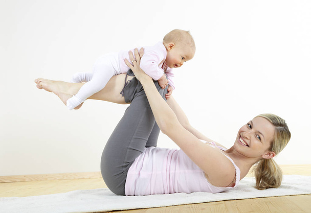 Healthy mother with her seven month old baby making gymnastics at home  - Foto, Bild