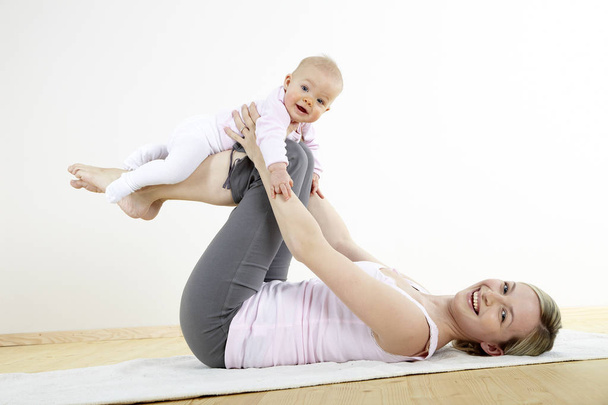young beautiful mother training body with her seven month old baby at home   - Photo, image