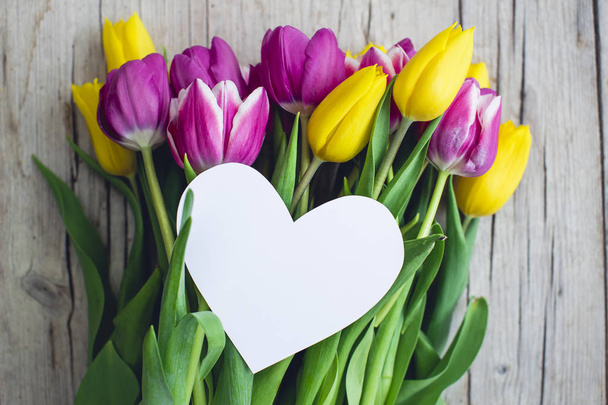 empty paper heart on bouquet of pink and yellow tulips on wooden background, mothers day concept - Zdjęcie, obraz