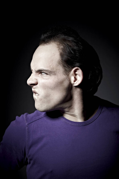 portrait of angry man in purple pullover looking aside  on dark background  - Фото, изображение