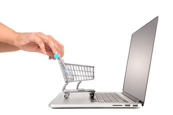 Mão empurrando um pequeno carrinho de compras em um laptop isolado em branco
 - Foto, Imagem