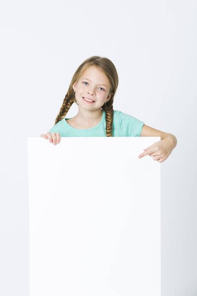 happy girl with braids in turquoise t-shirt smiling and pointing at empty board isolated on white background - Фото, зображення