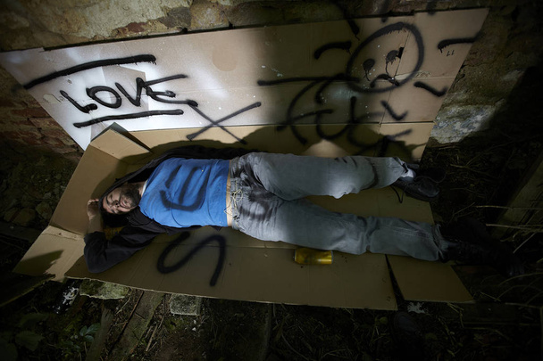 senzatetto in abiti scarabocchiati che dorme su scatole di cartone tra la spazzatura in un edificio abbandonato
  - Foto, immagini