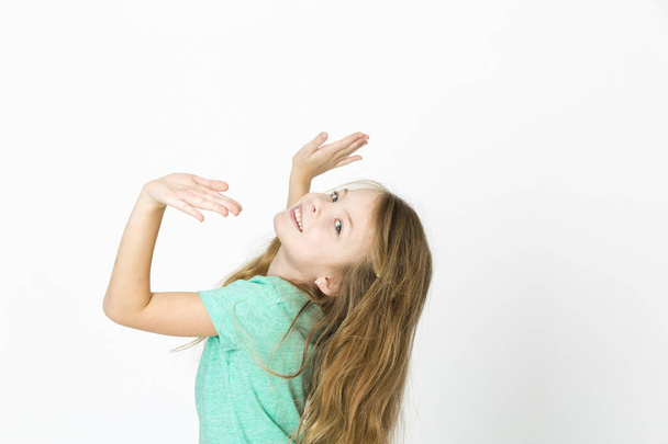 happy beautiful little blonde girl in green t-shirt dancing on white studio background  - Fotó, kép