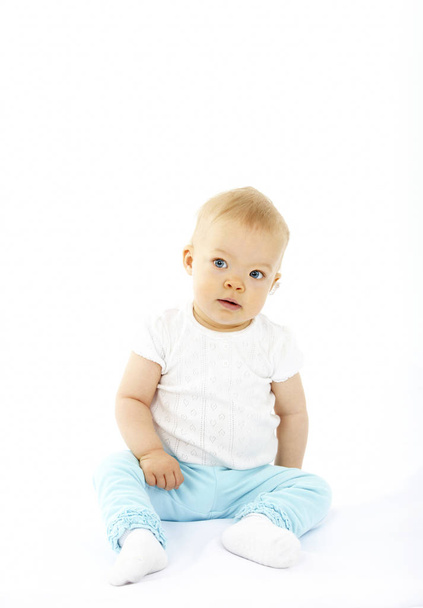 aranyos kis baba, fehér pólót és kék nadrágot ül míg jelentő elszigetelt fehér background - Fotó, kép