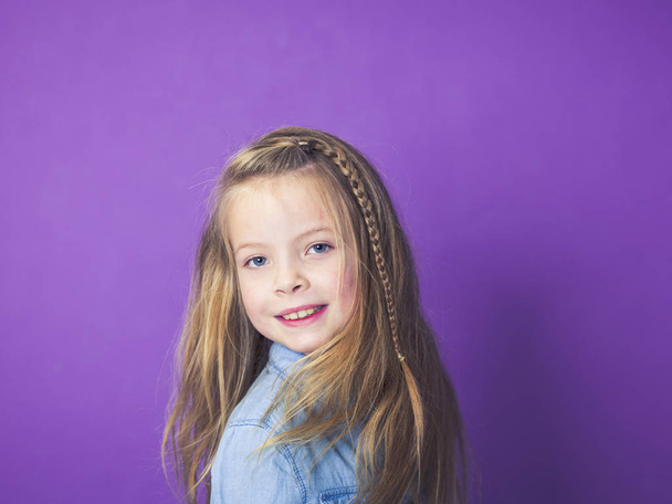 portrait of cute little girl wearing blue denim shirt in front of violet background in studio - Фото, изображение