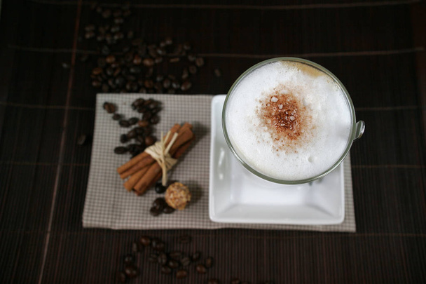 üveg ingerlékeny caffe latte a csészealj, kávé bab és a fahéjat, a tábla, közelkép  - Fotó, kép