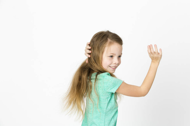happy beautiful little blonde girl in green t-shirt dancing on white studio background  - Фото, изображение