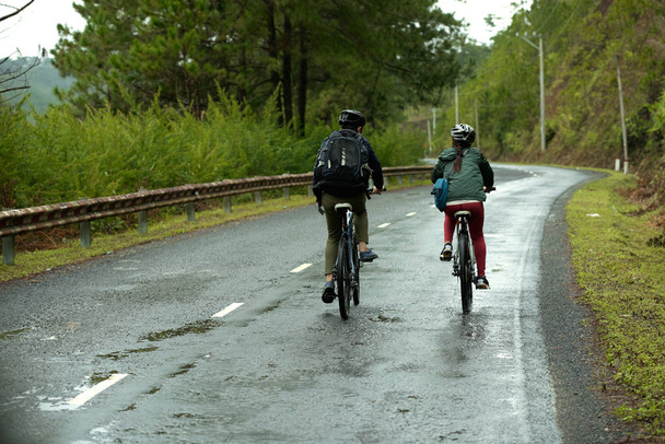 Vue arrière d'un couple roulant ensemble sur une route mouillée
  - Photo, image